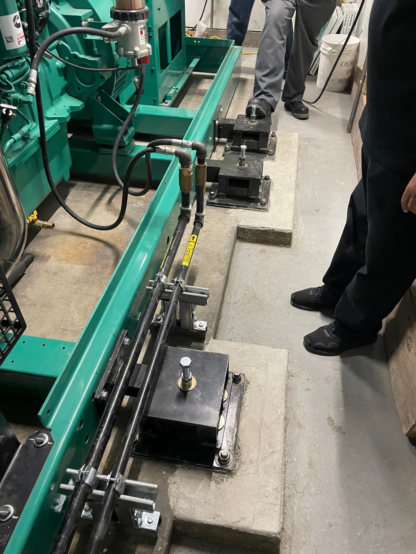 Restrained spring isolators with off-set support plates installed under an emergency generator skid on concrete housekeeping pads