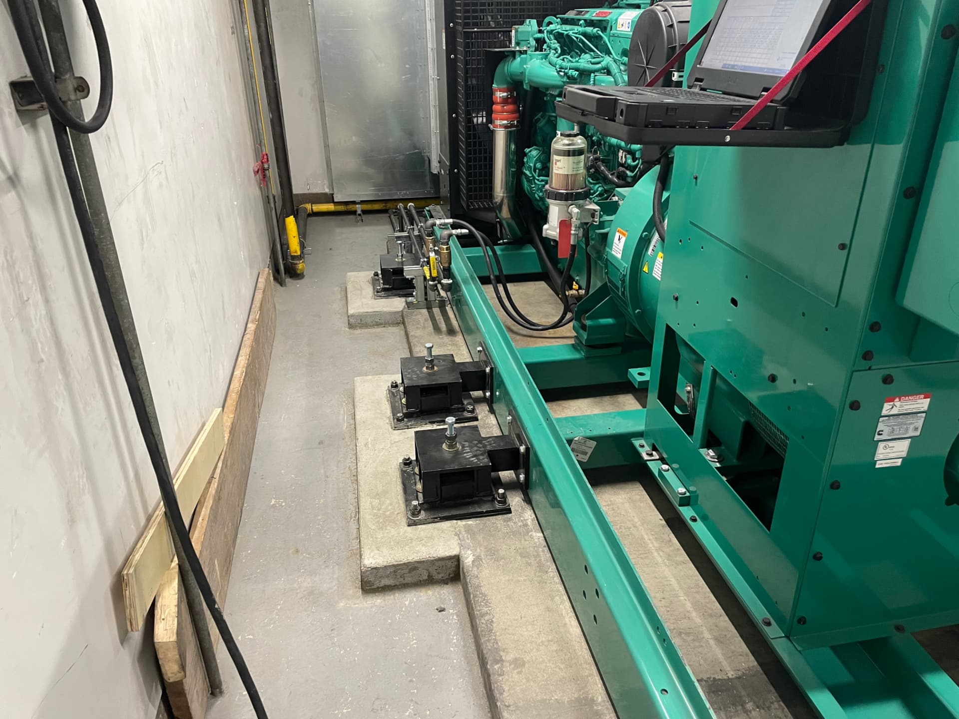 Row of off-set seismic mount isolators supporting a generator skid in a tight walk-in equipment room with limited side clearance